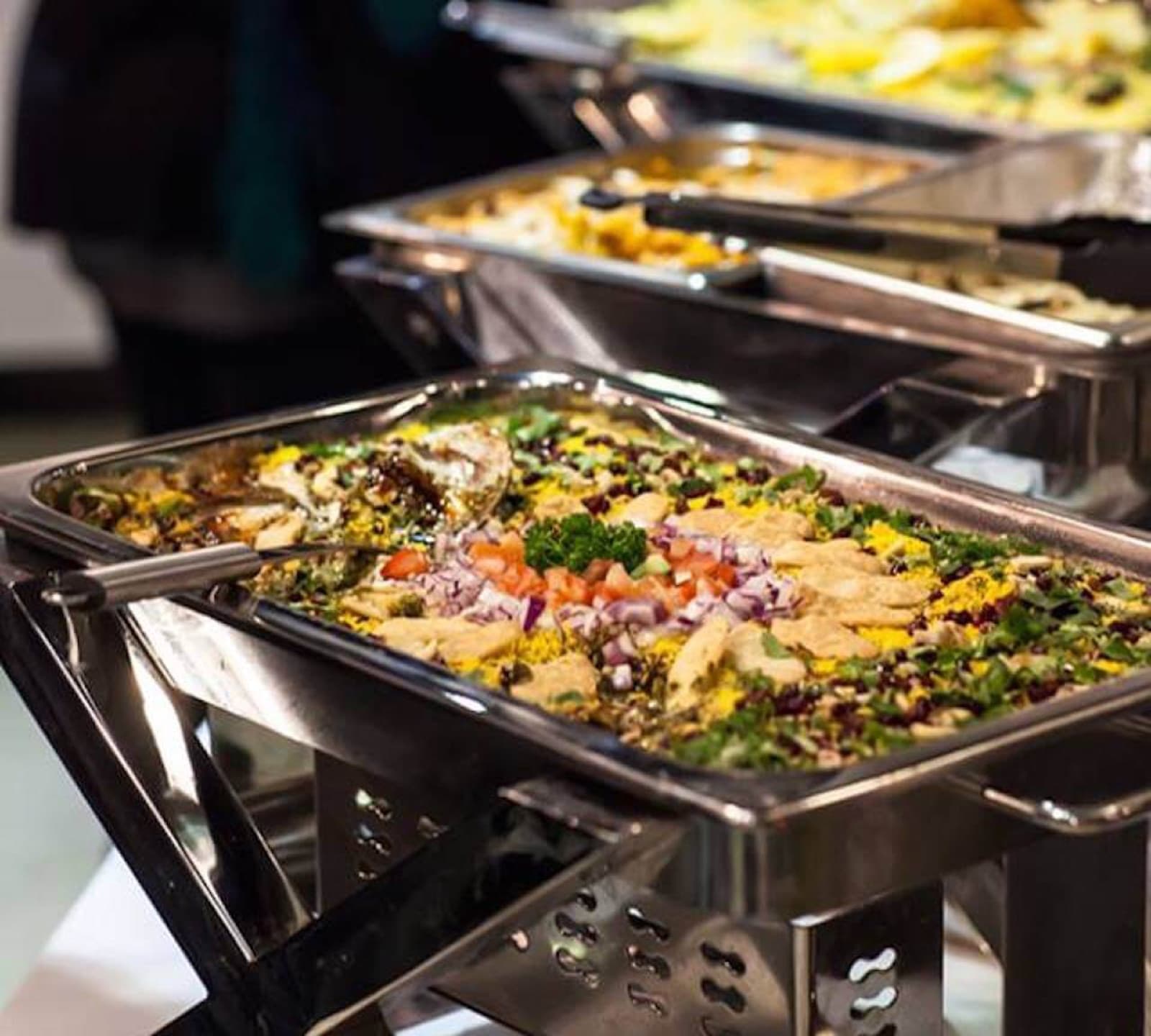 Chafing dishes lined up with a garnished rice and salad spread at a Dosa Hut catering setup